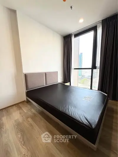 Modern bedroom with large window and city view, featuring sleek wooden flooring and minimalist design.