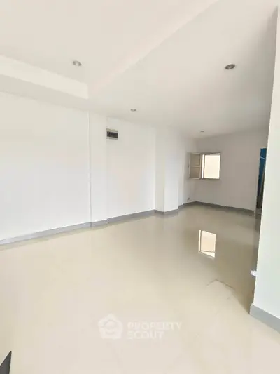 Spacious empty room with glossy tiled flooring and bright natural light.
