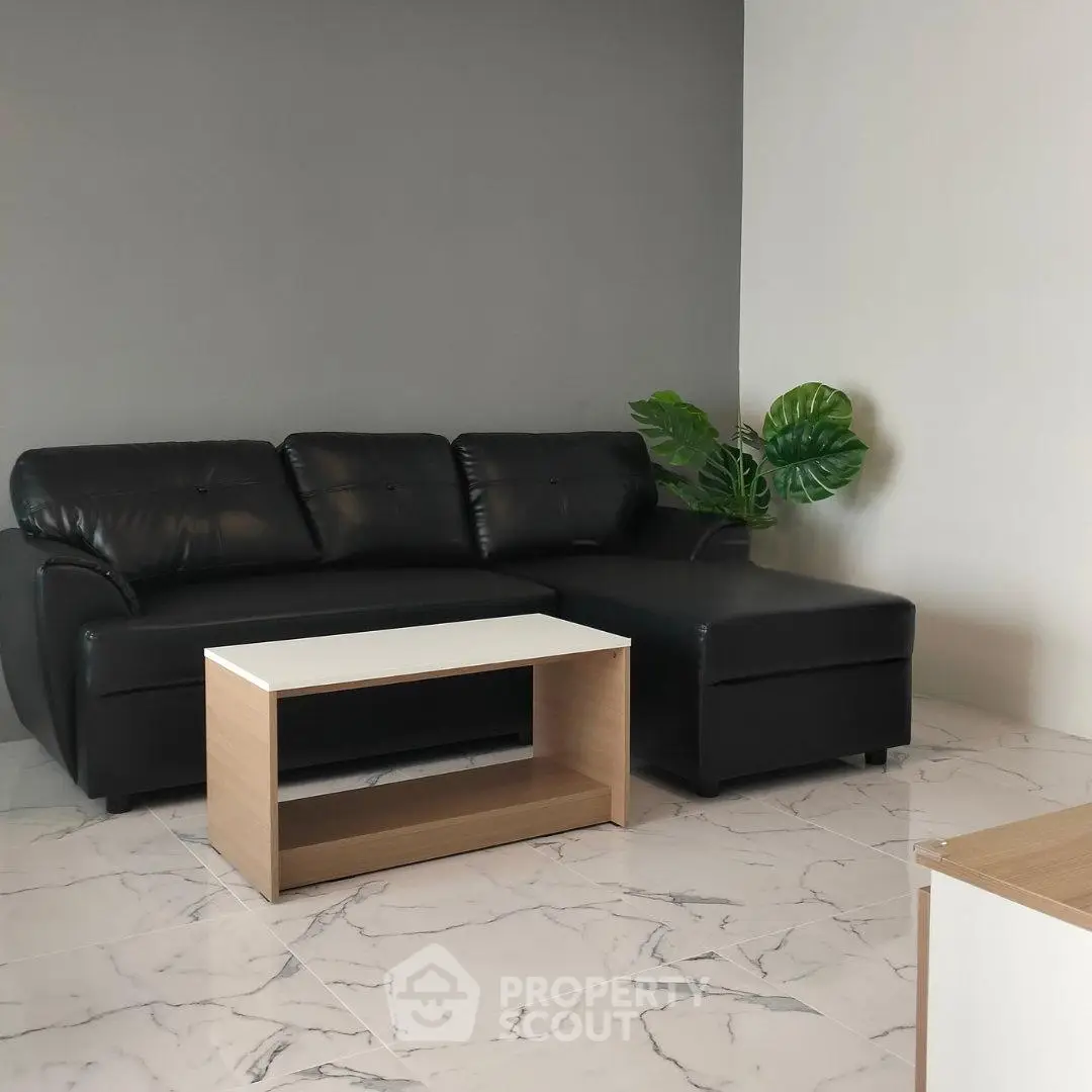 Modern living room with black leather sofa and sleek coffee table on marble floor.