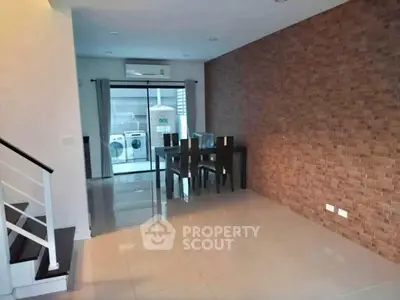 Modern dining area with exposed brick wall and view of laundry appliances.