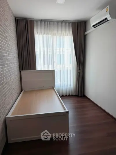 Cozy bedroom with wooden flooring and air conditioning, featuring a single bed frame and large window with curtains.