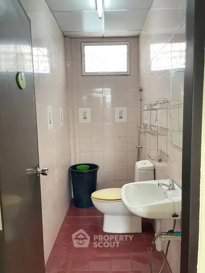 Compact bathroom with tiled walls, featuring a toilet, sink, and window for natural light.