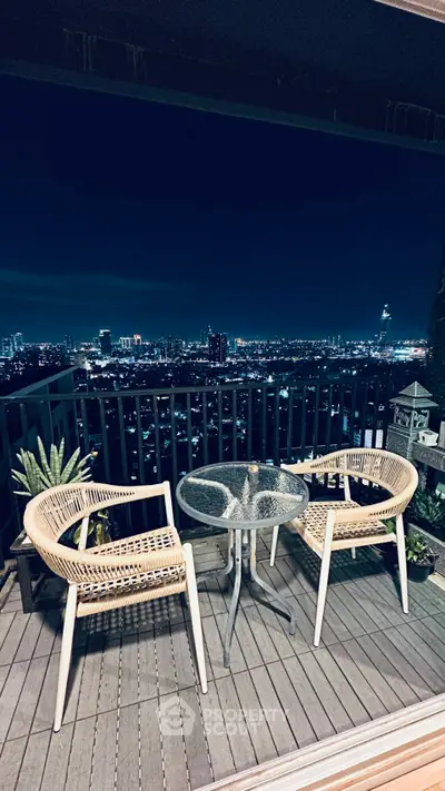 Stunning balcony view with cozy seating overlooking city skyline at night.