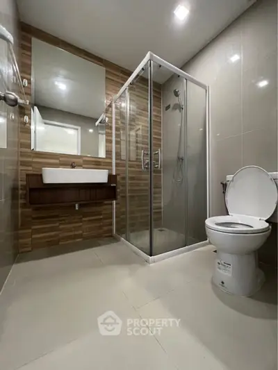Modern bathroom with sleek glass shower enclosure, wooden vanity, large mirror, and premium fixtures offering a luxurious and functional space.