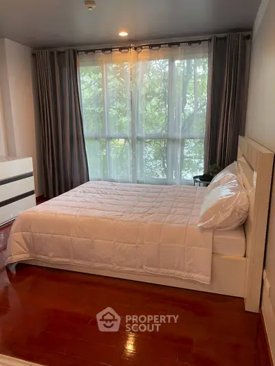 Spacious bedroom with large window and elegant curtains, featuring a cozy bed and polished wooden floor.