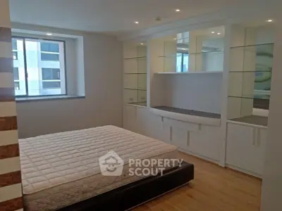 Spacious bedroom with built-in shelves and large window in modern apartment.