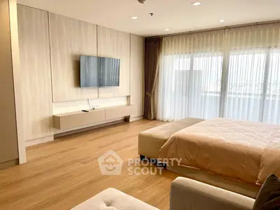 Spacious modern bedroom with large window and mounted TV, featuring elegant wood flooring.