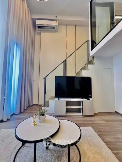 Modern living room with stylish staircase and large TV, featuring elegant decor and natural light.