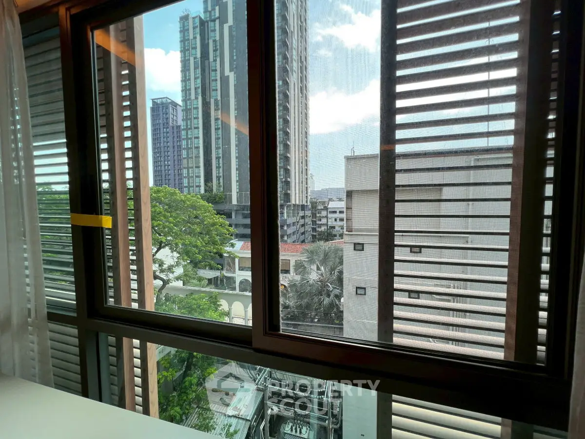 Stunning urban view from modern apartment window with cityscape and lush greenery.