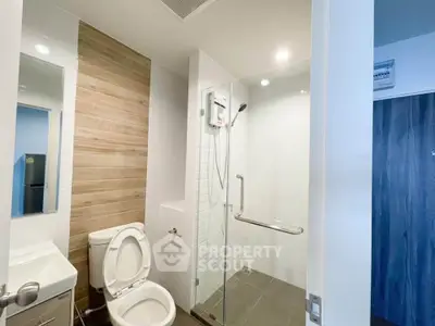 Modern bathroom with glass shower and wooden accent wall in sleek apartment.