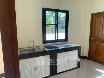 Modern kitchen with sleek black countertop and white cabinets, featuring a large window with garden view.