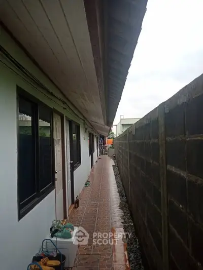 Narrow exterior corridor with tiled flooring and adjacent building wall.