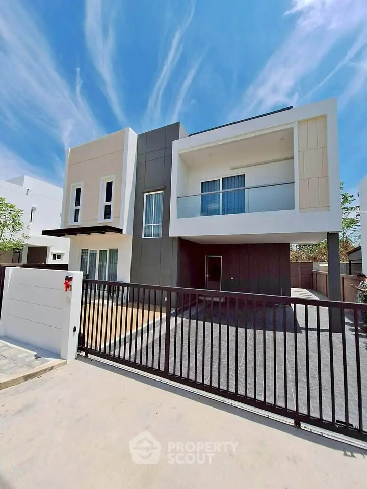 Modern two-story house with sleek design and spacious balcony under a clear blue sky.