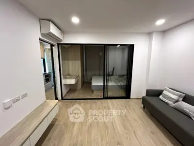 Modern apartment with open layout, featuring a cozy living area and a bedroom separated by glass doors.