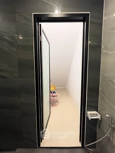 Modern bathroom with sleek black tiles and a frosted glass door leading to a storage area.