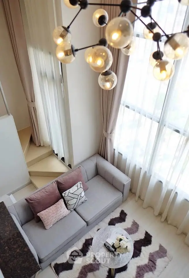 Elegant living room with high ceilings and modern chandelier, featuring a cozy sofa and large windows for natural light.