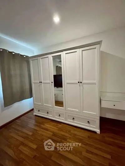 Spacious bedroom with elegant white wardrobe and wooden flooring.