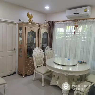 Elegant dining area with classic white furniture and ornate details, complemented by a sophisticated display cabinet and plush seating.