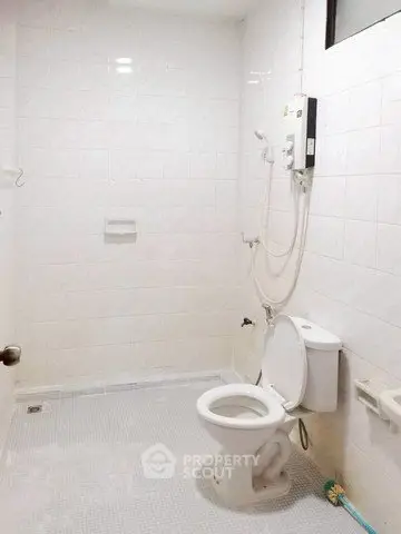 Spacious bathroom with modern fixtures and white tiled walls, featuring a shower and toilet.
