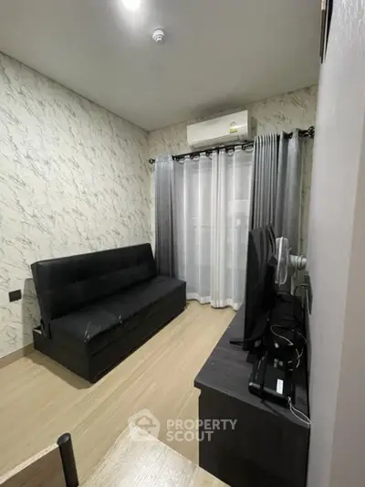 Modern living room with sleek black sofa and wall-mounted TV, featuring stylish decor and natural light.