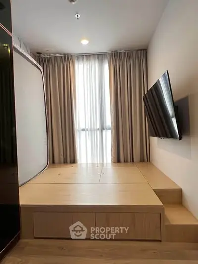 Modern minimalist living room with platform bed and wall-mounted TV, featuring elegant curtains and wooden flooring.