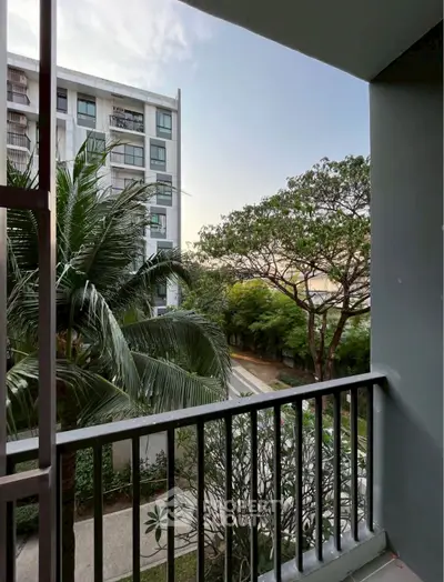 Charming balcony view with lush greenery and modern building backdrop.