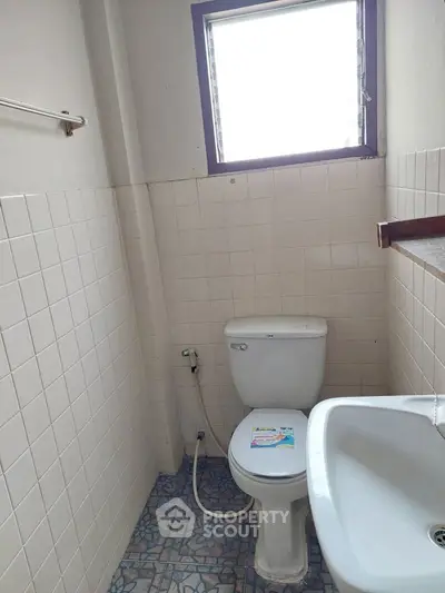 Compact bathroom with tiled walls and floor, featuring a toilet and sink under a window.
