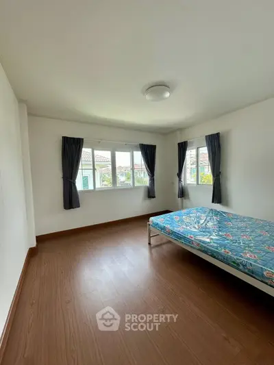Spacious bedroom with large windows and wooden flooring in a modern home.