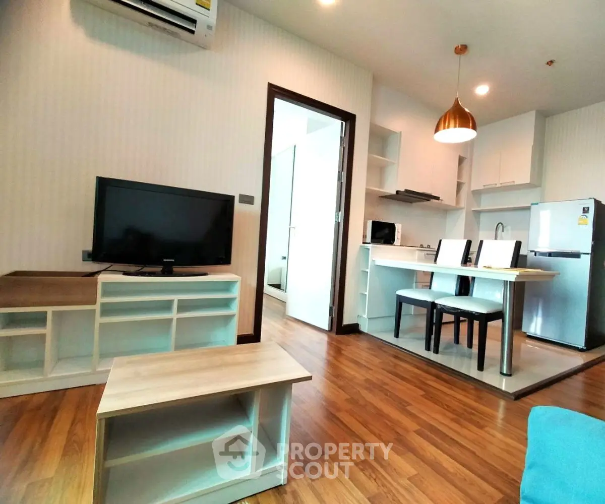 Modern open-plan living room with kitchen, featuring wooden floors and stylish lighting.