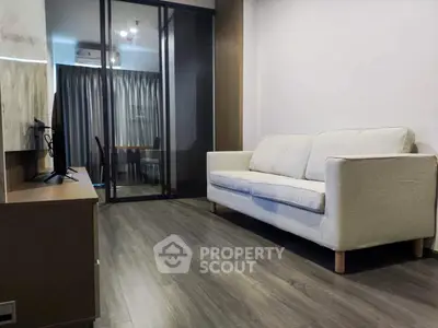 Modern living room with sleek wooden flooring and cozy white sofa, featuring a glass partition leading to a study area.