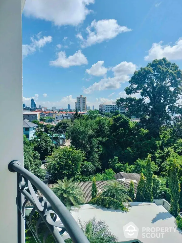 Stunning cityscape view from a balcony with lush greenery and clear blue skies.