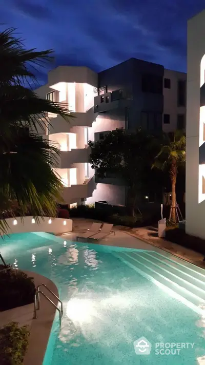 Stunning nighttime view of modern apartment complex with illuminated pool and lush greenery.