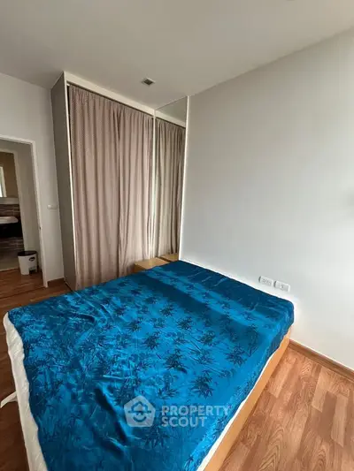 Cozy bedroom with wooden flooring and mirrored wardrobe, featuring a plush blue bedspread for a serene ambiance.