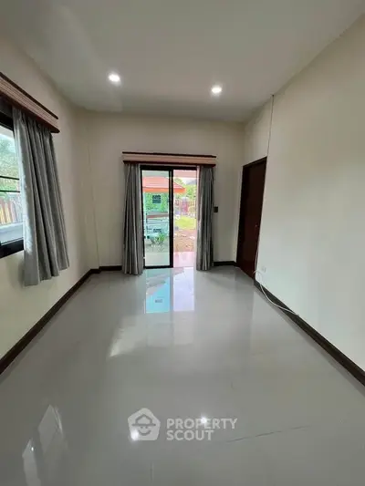 Spacious empty room with glossy tiled floor and sliding glass doors leading to a garden view.
