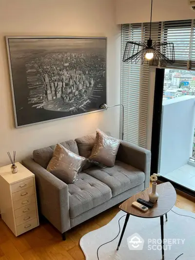 Chic urban living room with stylish grey sofa, modern art, and a unique light fixture, complemented by a city view through large windows.