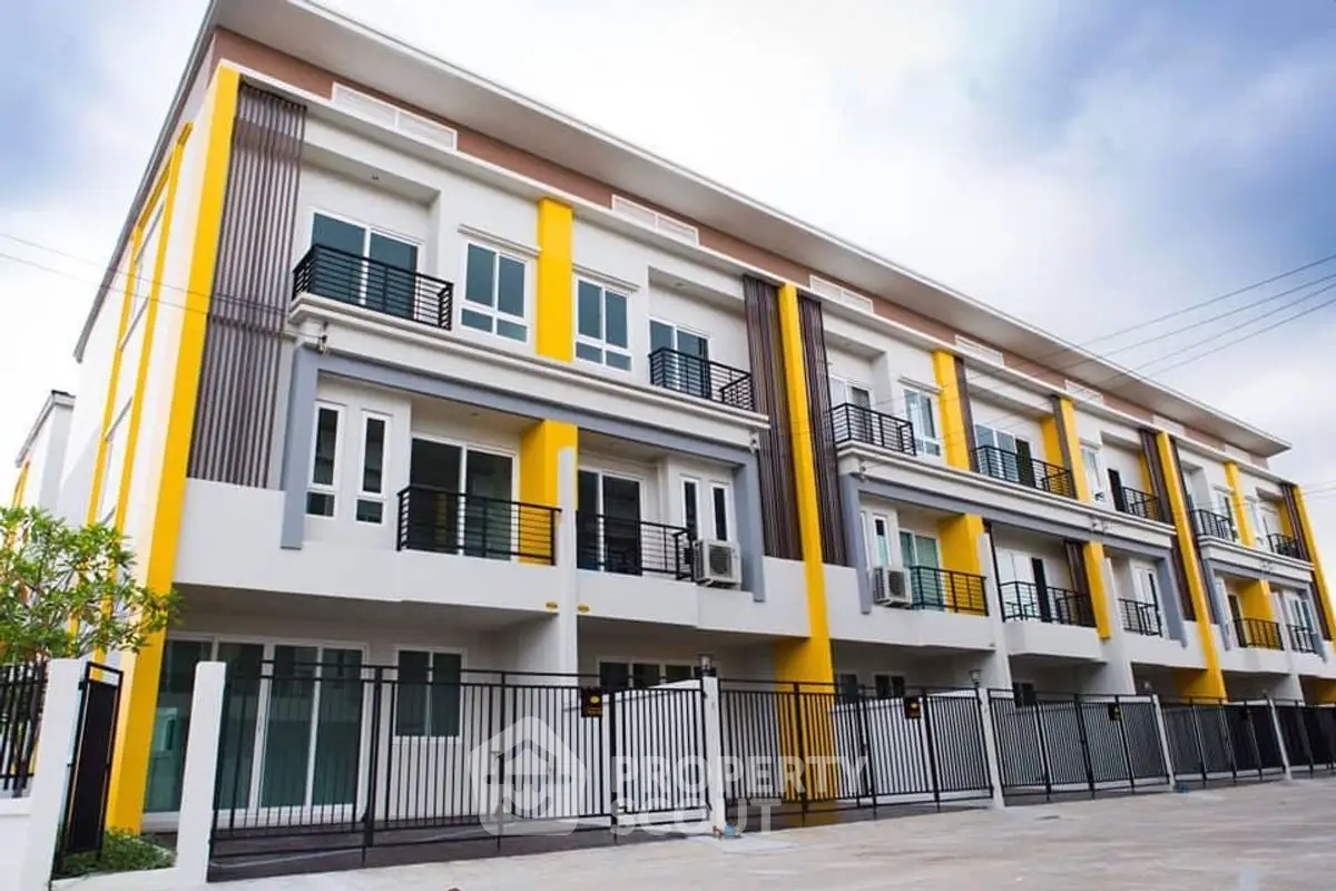 Modern multi-story townhouse with vibrant yellow accents and secure gated entrance.