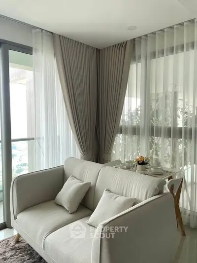 Elegant living room with cozy sofa and dining area near large windows with sheer curtains.