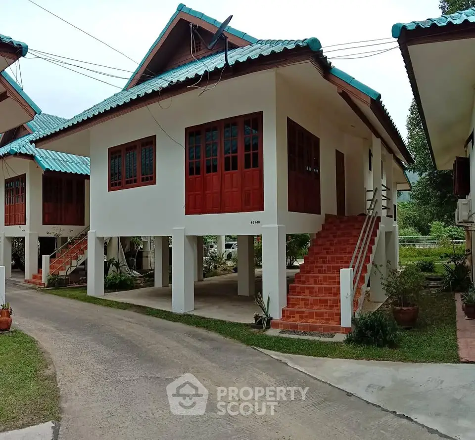 Charming elevated house with red accents and blue roof in serene neighborhood