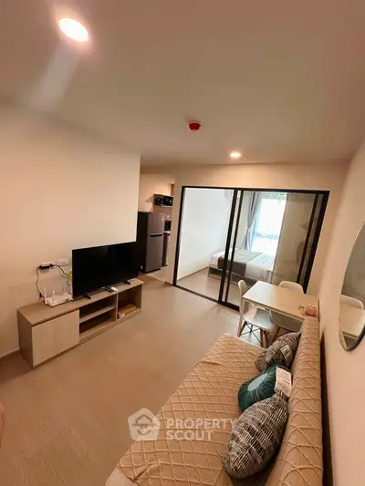 Modern living room with cozy sofa, TV, and dining area leading to a bedroom with glass sliding doors.