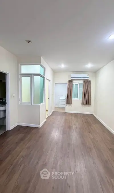Spacious empty room with wooden flooring and large window, perfect for customization.