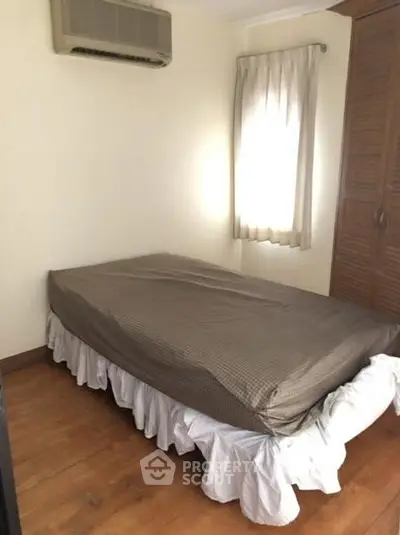 Cozy bedroom with wooden flooring and air conditioning unit, featuring a comfortable bed and ample natural light.
