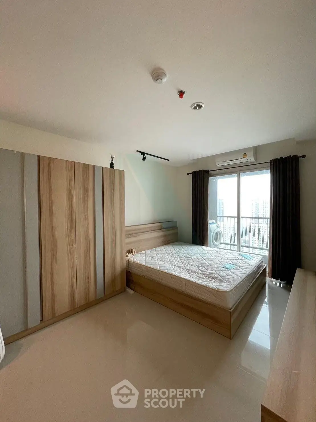 Spacious bedroom with large window and city view, featuring modern wooden furniture and ample natural light.