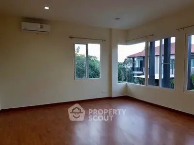 Spacious empty room with wooden flooring and large windows offering natural light and garden view.
