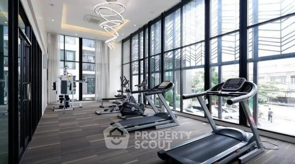 Modern gym with large windows and state-of-the-art equipment in luxury building.