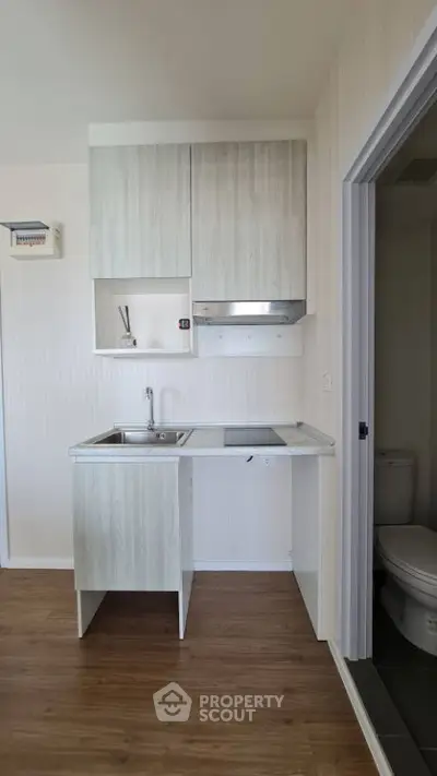 Compact kitchen with modern cabinetry and adjacent bathroom in cozy apartment