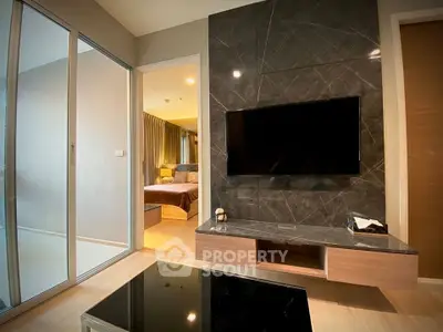 Modern living room with sleek TV wall and view into cozy bedroom