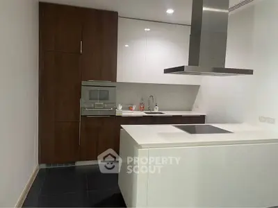 Modern kitchen with sleek cabinetry and island, featuring built-in oven and induction cooktop.