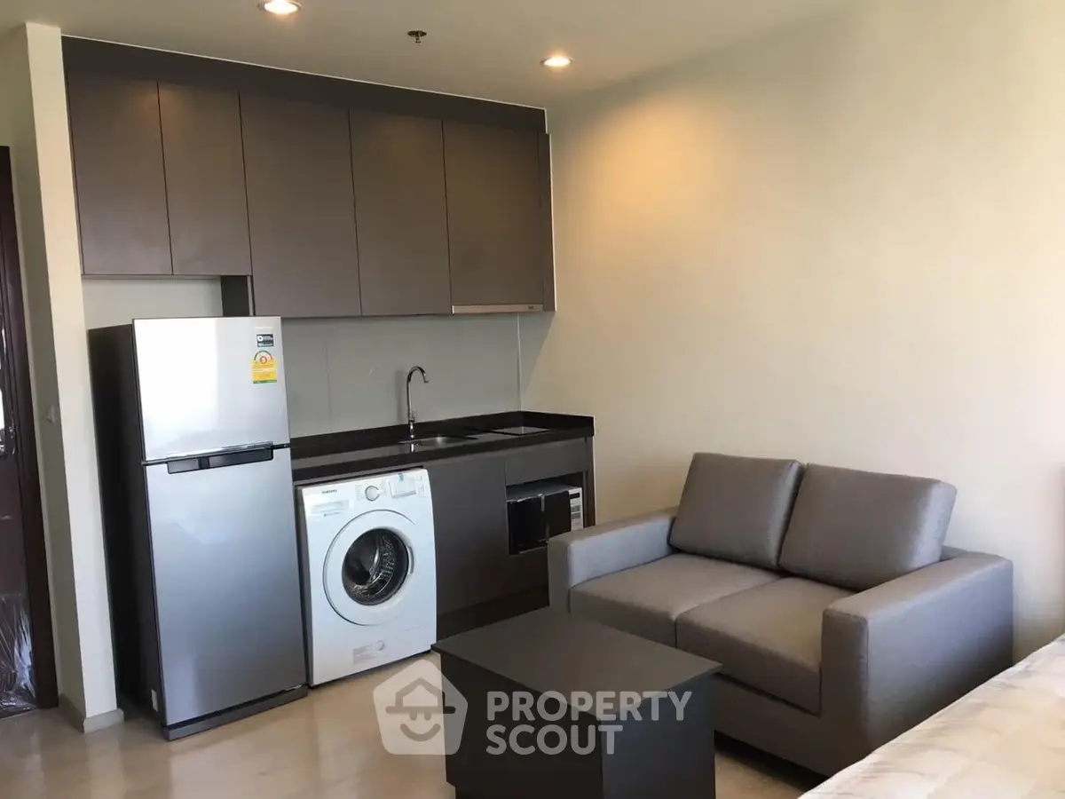 Modern studio apartment with compact kitchen and cozy living area featuring a washing machine and sleek appliances.