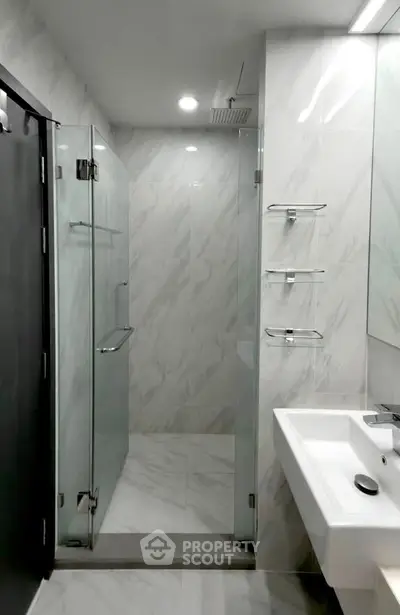 Modern bathroom with glass shower enclosure and sleek white sink in a contemporary apartment.