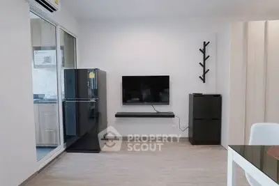 Modern living room with sleek black furniture and wall-mounted TV, adjacent to a compact kitchen.